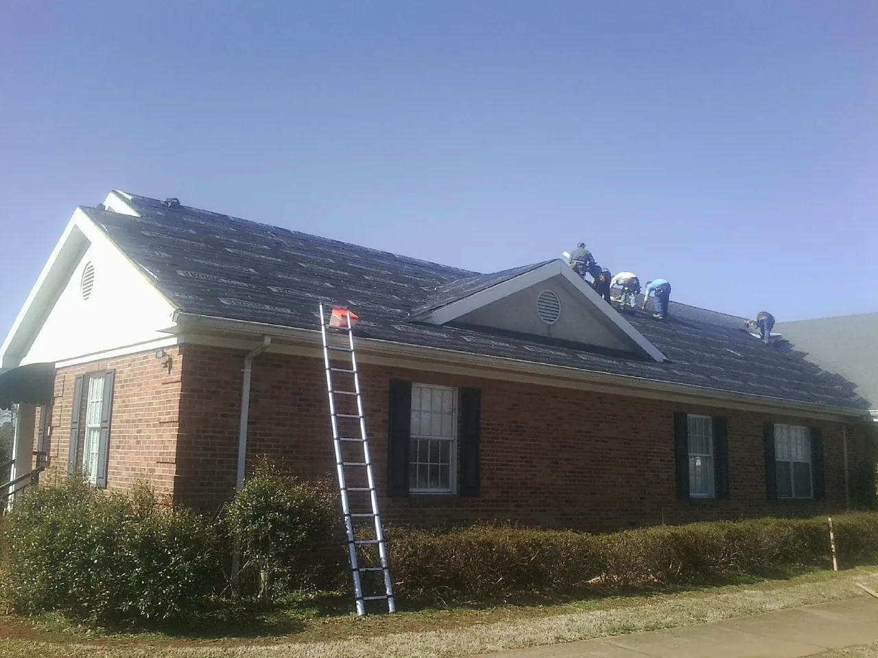 Crew tearing shingles off a brick ranch roof with a ladder set — Emergency Roof Repair work by our crew in Buena Vista
