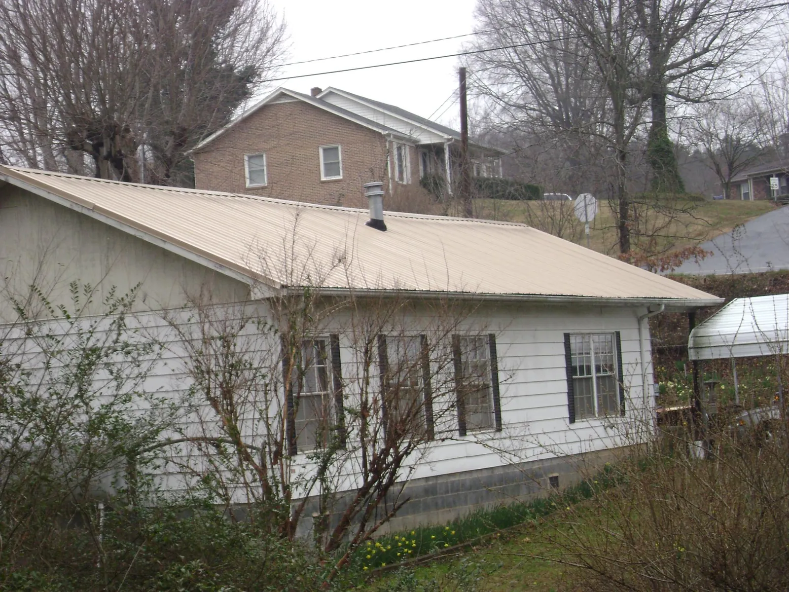 Tan metal roof on a white sided house set into a hillside — Commercial Roofing by Roofing Brothers in Buena Vista